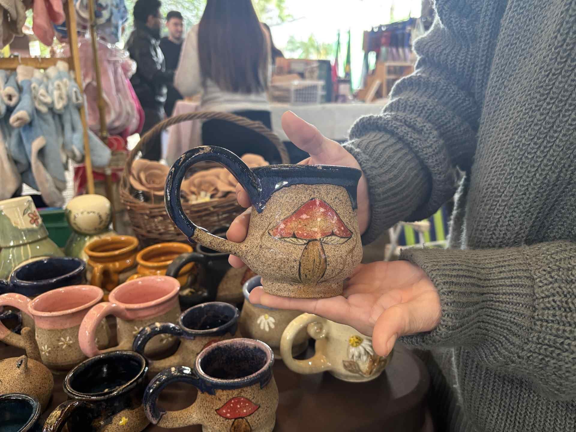 Caneca de cogumelo em grés, moldada à mão, nas mãos de uma visitante da feira